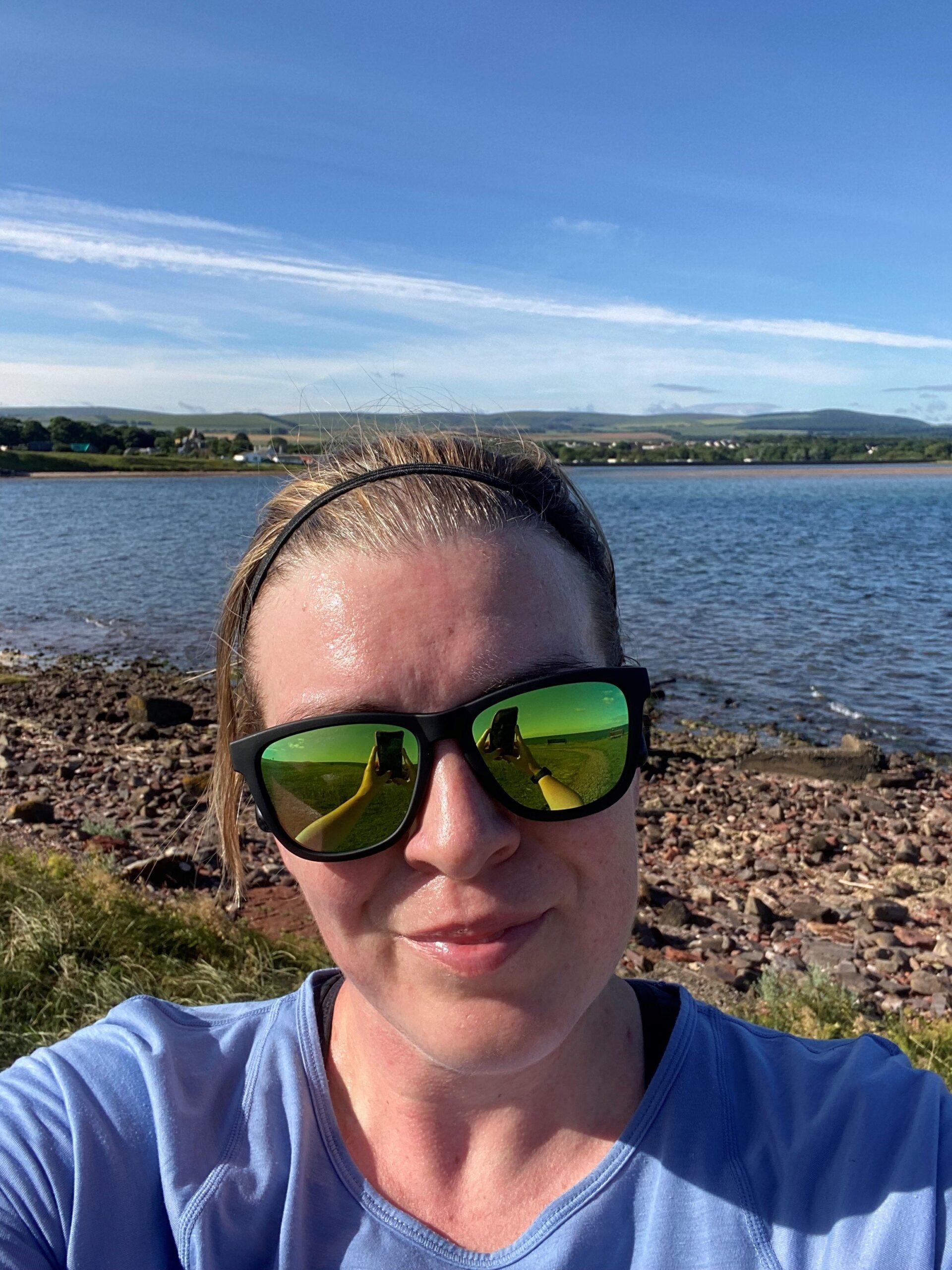 Selfie photo by a lake of a woman in sunglasses smiling at the camera