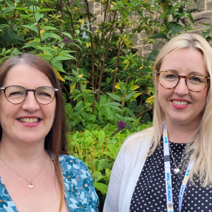 Two women smiling at camera with a leafy background